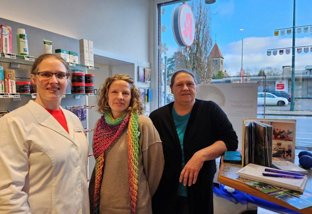 Zwei Mitarbeiterinnen der Diakonie Tagespflege Laggenbeck und Apothekerin Elena Beermann stehen an einem Infostand in der St.-Barbara-Apotheke und informieren Besucherinnen und Besucher über das Angebot der Tagespflege.