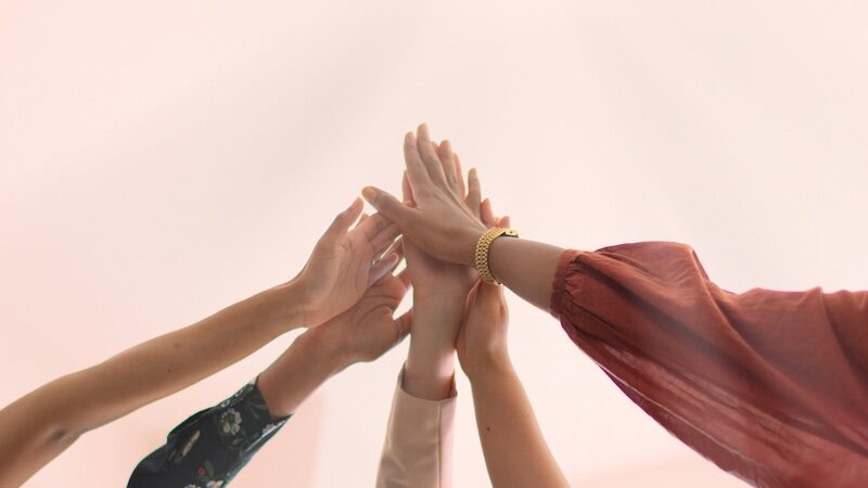 Eine vielfältige Gruppe von Frauen feiert Teamarbeit mit High-Fives. 